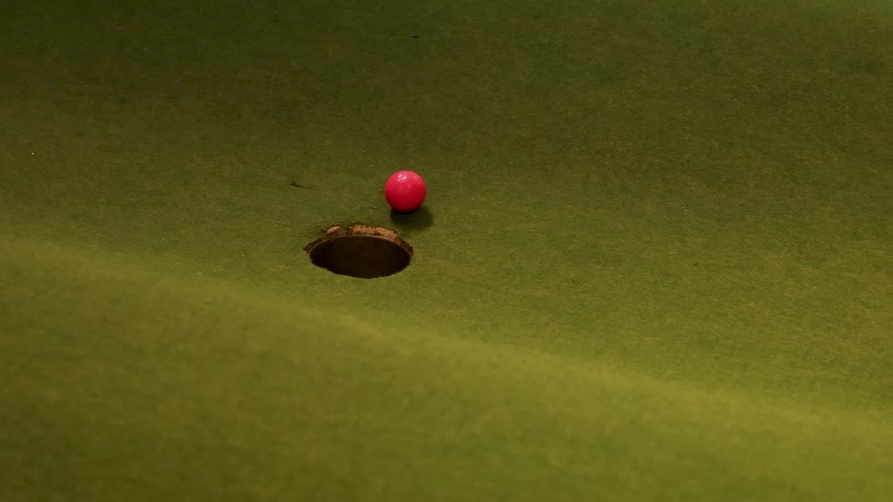 A red ball rolls towards a hole on a green surface, showcasing precision and movement.