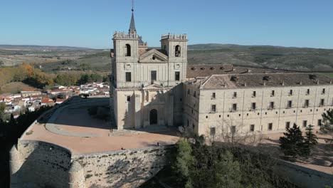 Reverse-flight-at-the-Uclés-monastery-contemplating-its-west-façade-with-the-entrance-portico-of-the-church-of-Nuestra-Señora-de-la-Asunción,-below-which-the-gardens-appear-in-the-province-of-Cuenca