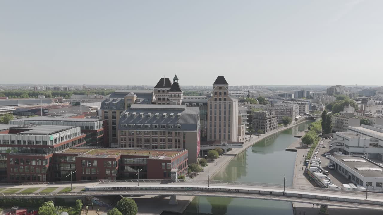 Fixed aerial drone shot of the Grands Moulins de Pantin with the Canal de l’Ourcq, a small bridge, and the Pantin district - France