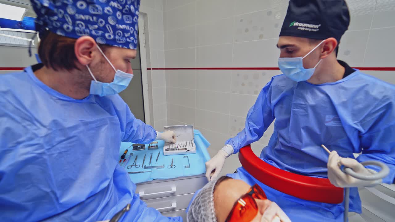 Dentist performing dental surgery. Two male dentist in uniform perform dental operation on patient at dentistry office