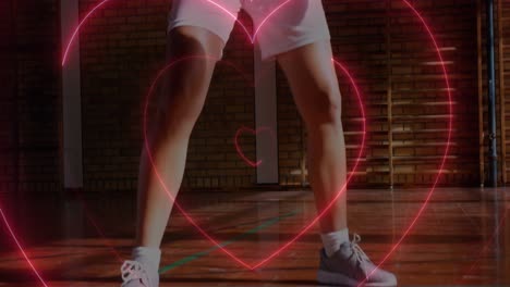 animación de corazones de neón sobre una jugadora de baloncesto caucásica rebotando la pelota