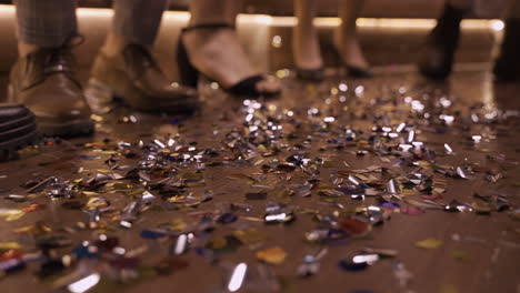 camera focuses on the wooden floor full of confetti and men shoes and women heels moving while they dance