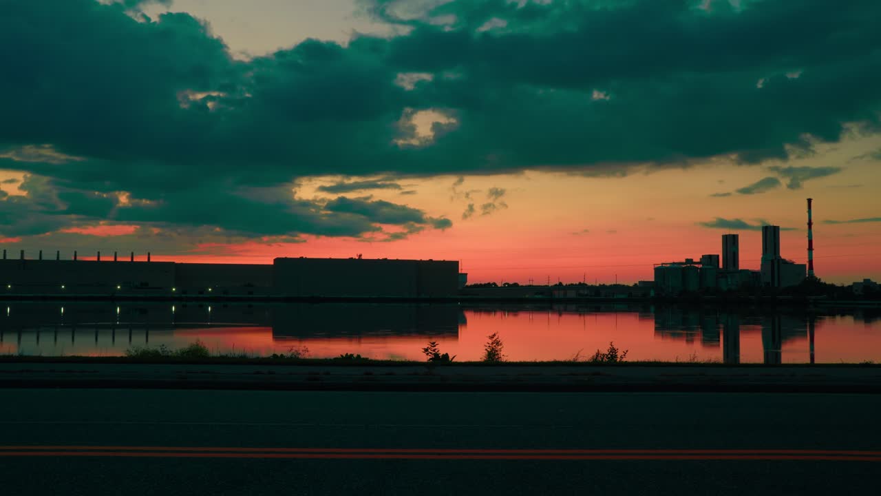 Industrial paper mill at sunset in Wisconsin Rapids, reflecting in calm water under moody clouds. Cinematic time-lapse day to night