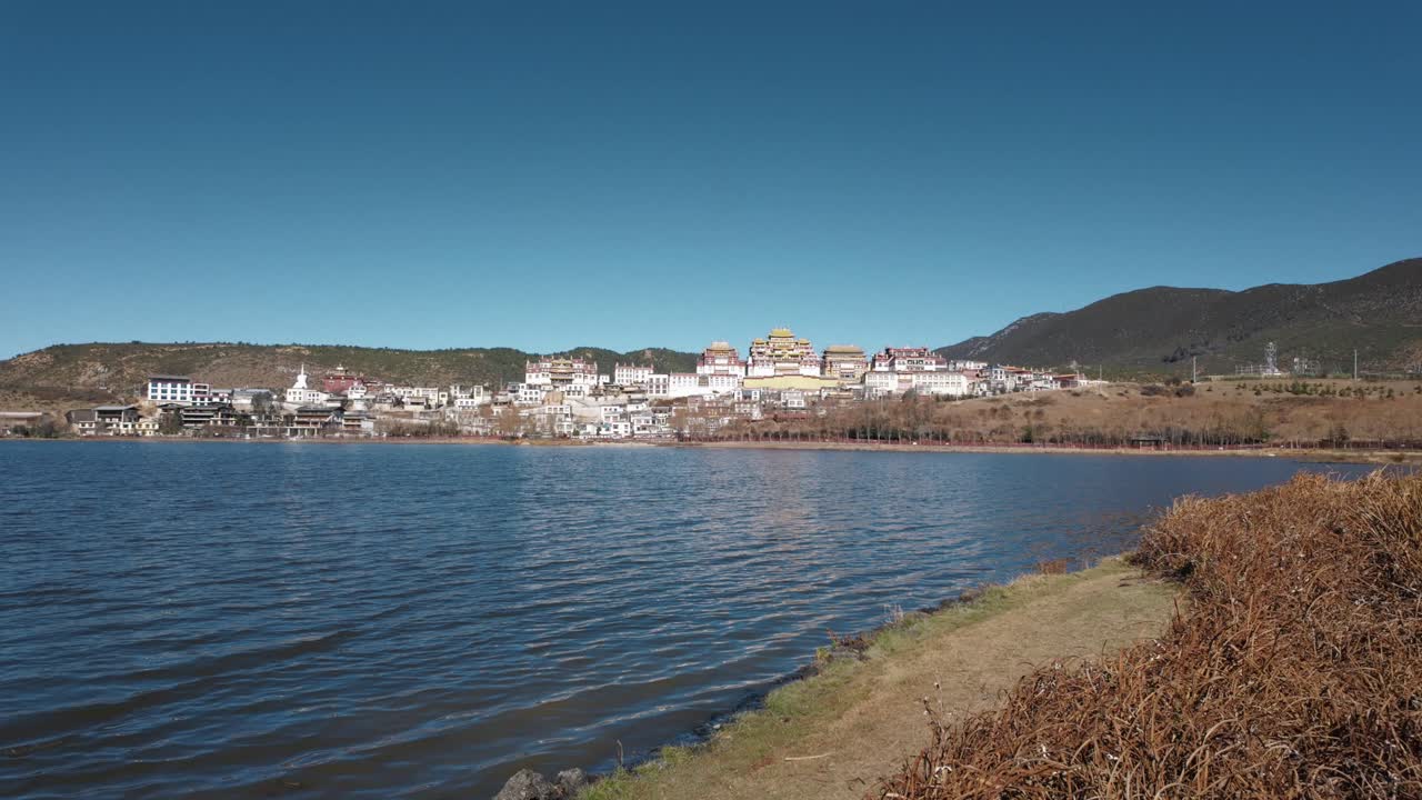 Görkemli Songzanlin Manastırı, Shangri-La'da sakin bir gölün üzerinde yükselerek, berrak gökyüzü ve dağ manzarasına karşı ikonik Tibet mimarisini sergiliyor.