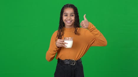 teen african american girl drinking milk showing thumb up looking at camera smiling. portrait of happy satisfied teenager drinks healthful vitamin dairy on green screen chromakey.