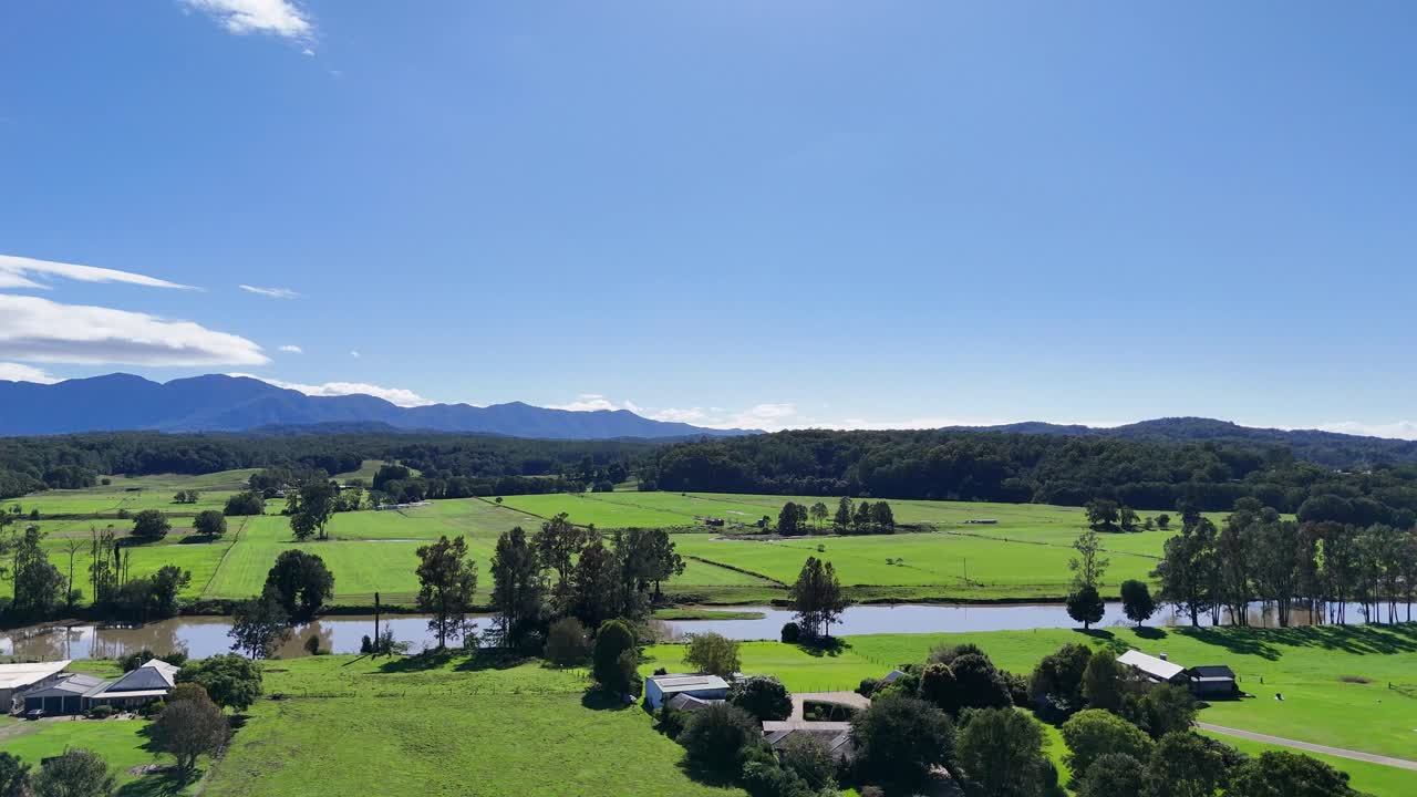 Aerial footage captures expansive green fields and distant mountains under clear blue skies in Dorrigo, NSW, Australia
