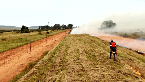 aerial tracking of farmworker burning dry grass between rural farms with torch