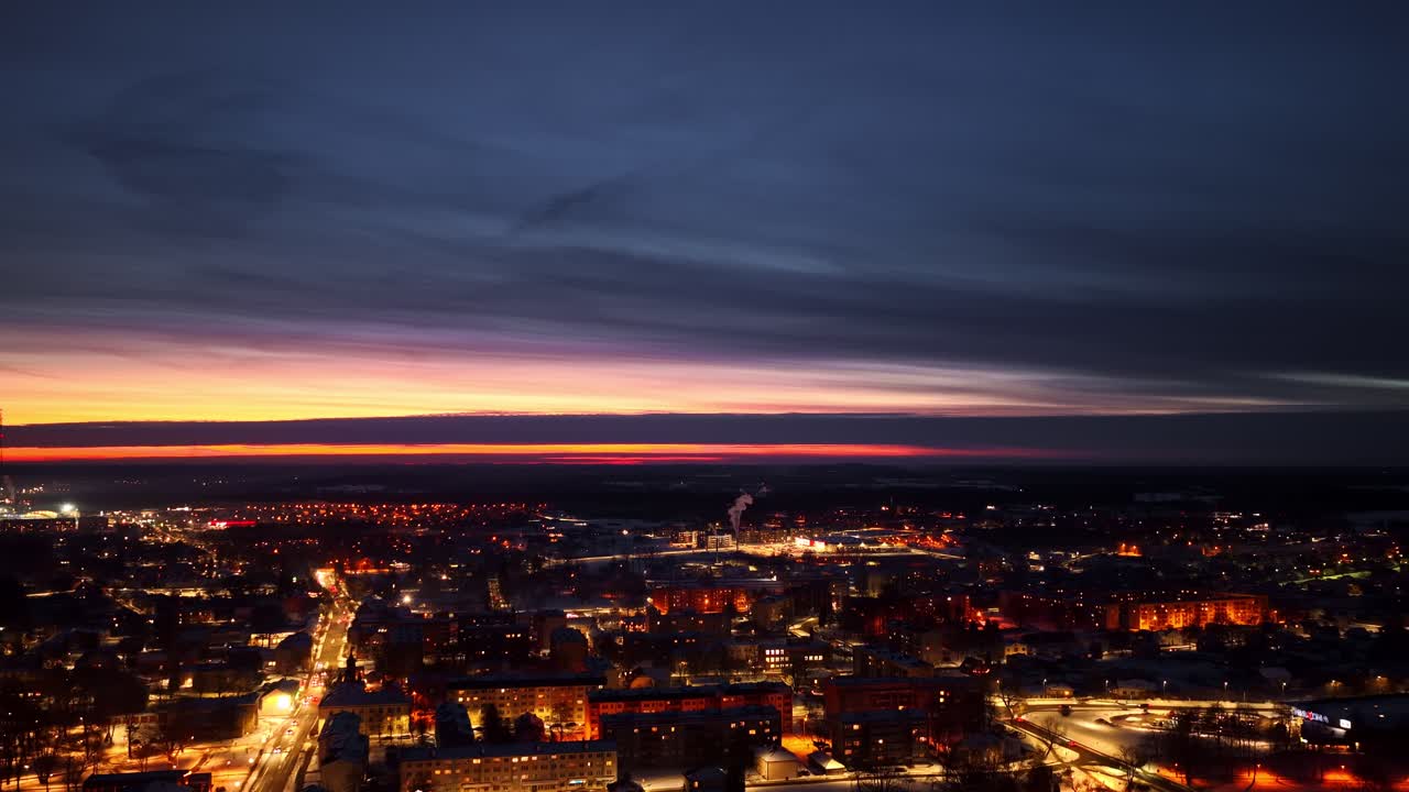 Luces de la ciudad iluminando edificios y carreteras bajo un cielo crepuscular colorido, vista aérea