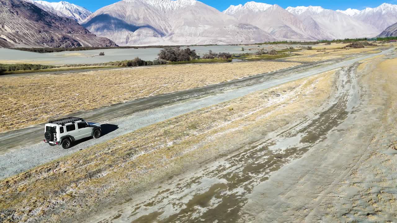 Aerial drone shot showcasing a car navigating through the contrasting terrain of Nubra Valley, where desert meets greenery.