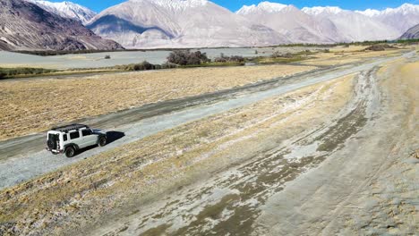 aerial drone shot showcasing a car navigating through the contrasting terrain of nubra valley, where desert meets greenery.