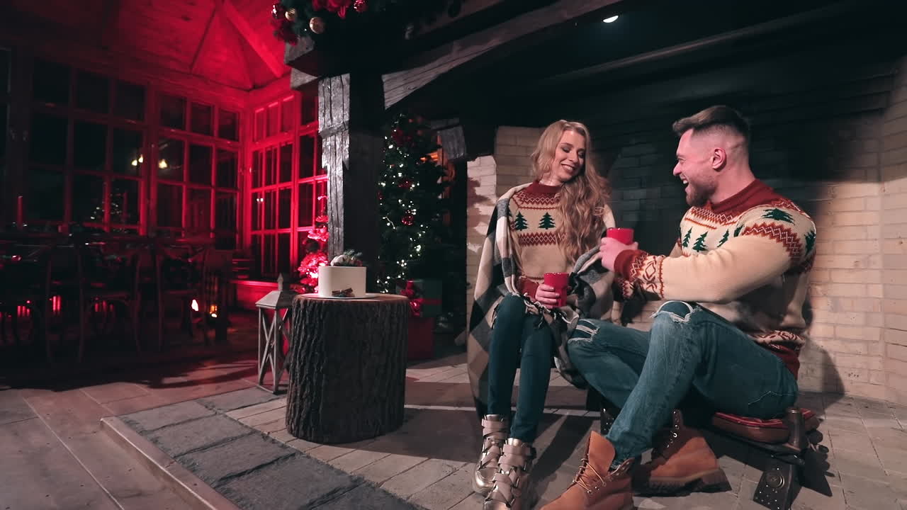 Happy young couple in love in Christmas sweaters at home. Handsome man and beautiful woman sitting in a country house and having joyful time together.