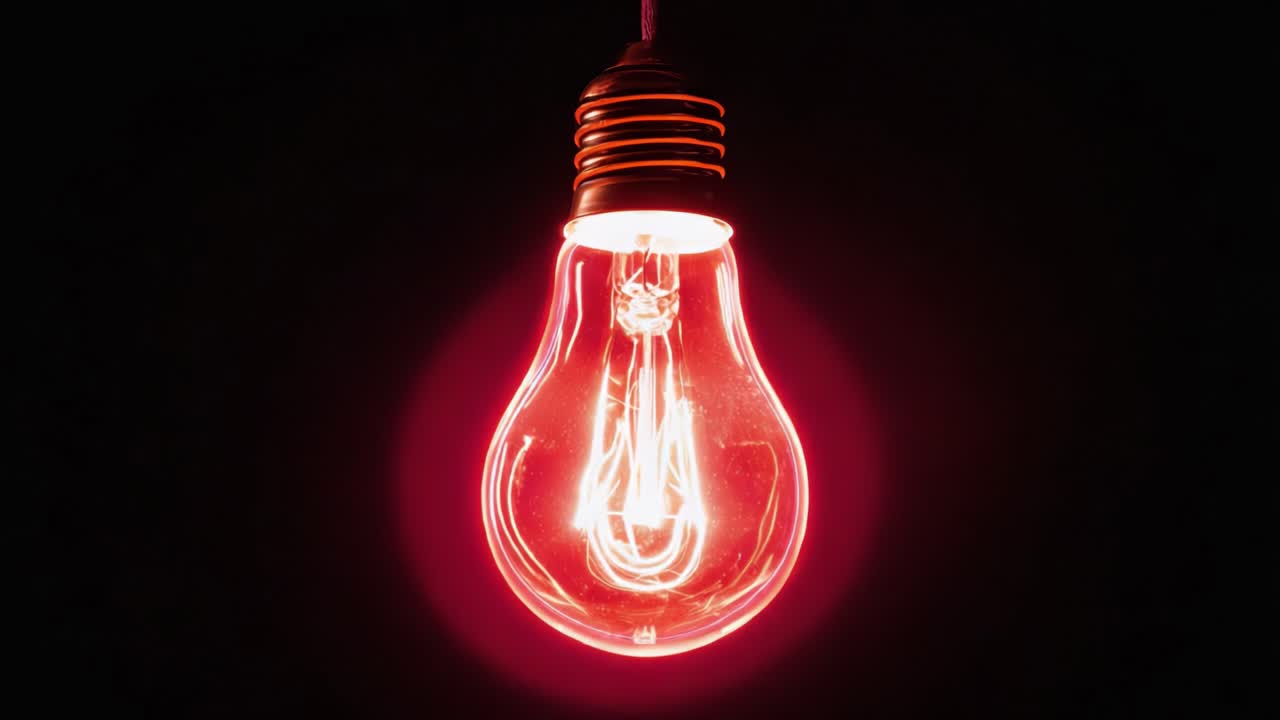 Red incandescent light bulb with a glowing tungsten filament turning on and off against a black background. Glowing halo effect represents idea, innovation, energy, and creativity