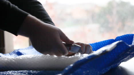 manos masculinas usando un cuchillo de corte para abrir un paquete envuelto en burbujas