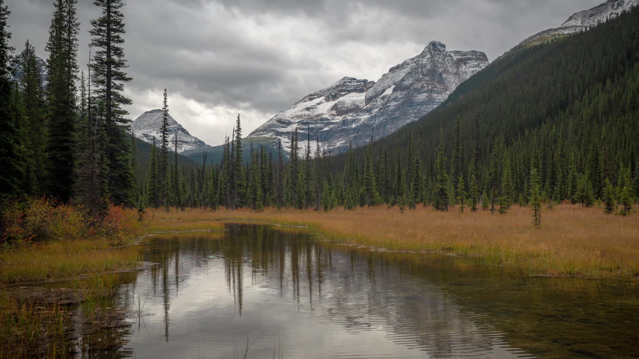 lapso de tiempo, frío día de otoño en las montañas de canadá, dramáticas nubes oscuras sobre cumbres cubiertas de nieve y valle con bosque de coníferas y agua de estanque