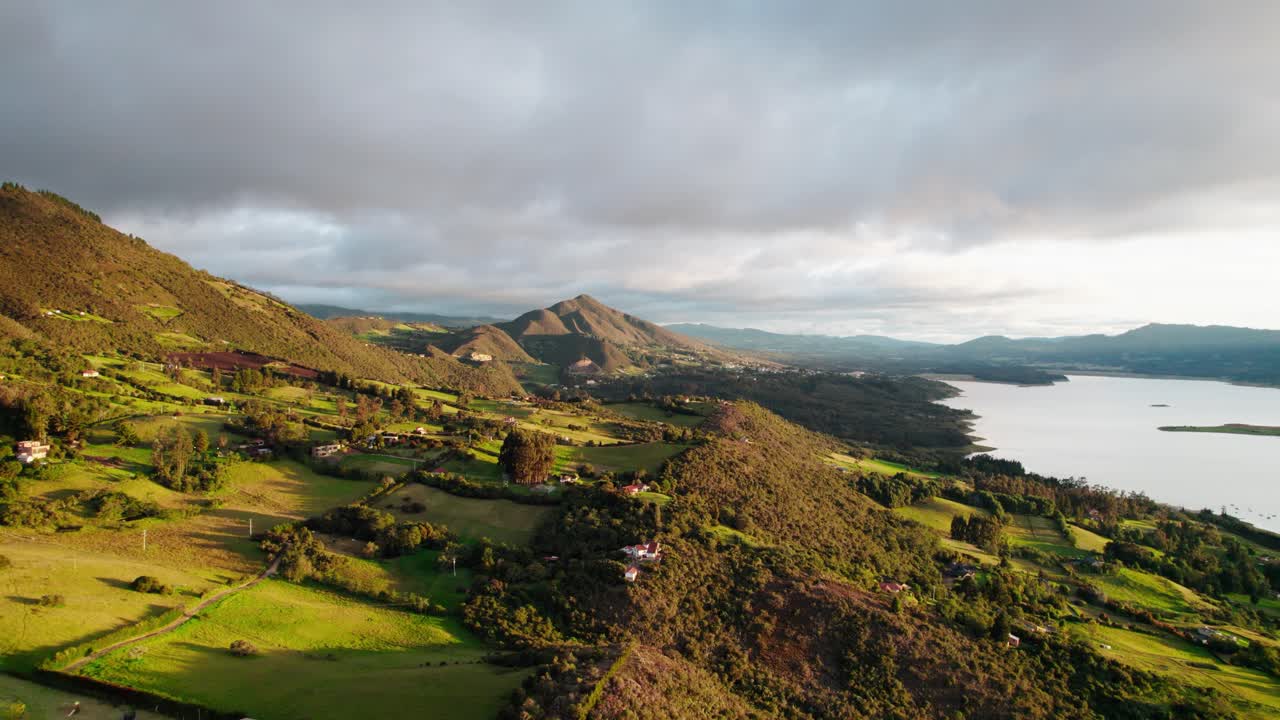 Drone zoom in over the vibrant rural landscape of Guatavita, Colombia, during golden hour, revealing hills, mountains, and the lake