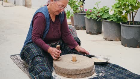 the old woman is grinding flour in the stone mill with the old traditional method. millstones for grinding wheat into flour, mill traditional production.