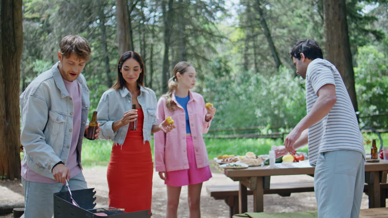 Young people enjoying barbecue at forest picnic. Two men two women socializing