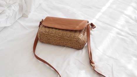 brown straw crossbody bag on a white bed