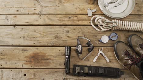 Camping-equipment-with-rope,-torch,-boots-and-copy-space-on-wooden-background