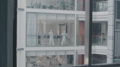 vista desde el exterior de dos hombres de limpieza que usan equipo de protección personal limpiando cristales dentro de un edificio de oficinas 1