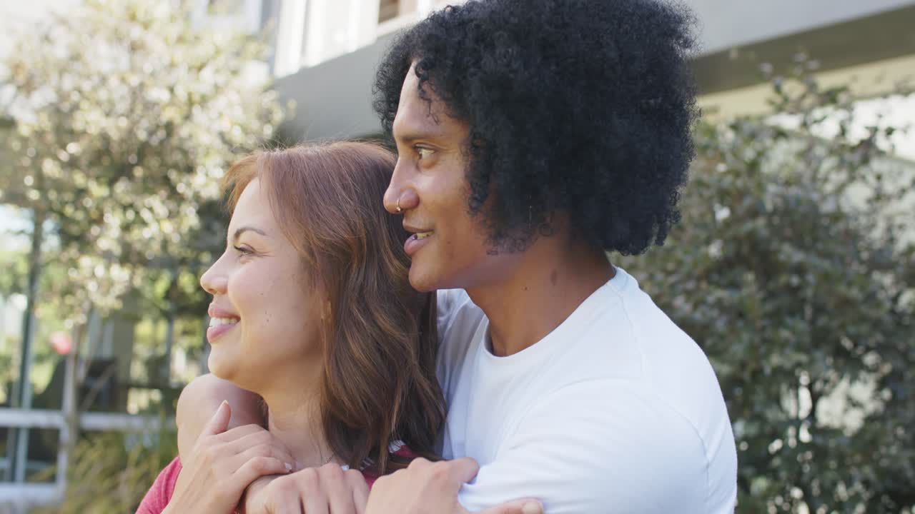 Coppia afroamericana che si abbraccia fuori casa, l'uomo l'avvolge con le braccia, ridendo e mostrando amore.