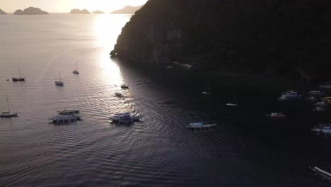 4k aerial drone shot of tour and fishing boats in the bay during sunset at corong corong beach in el nido, palawan, philippines