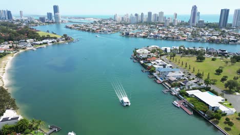 Canal-ferry-touring-past-million-dollar-mansions,-with-the-iconic-Surfers-Paradise-skyline-in-the-distance,-4K-drone-footage