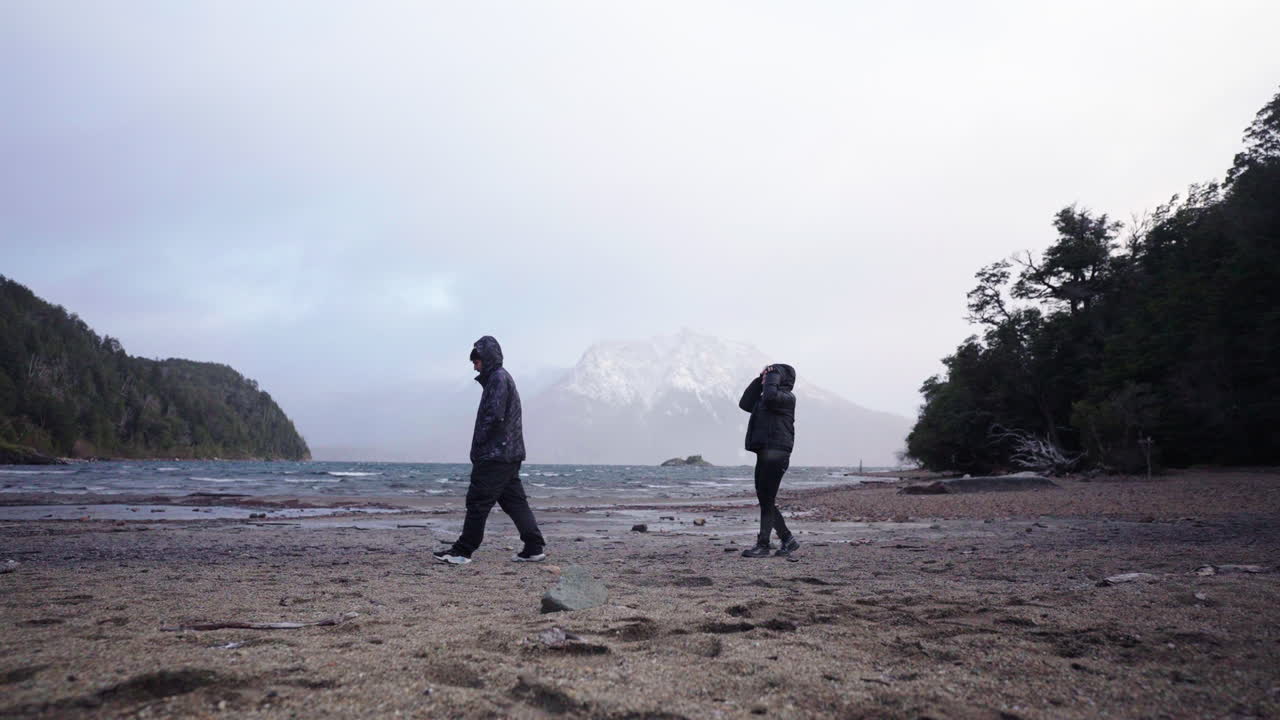 Two people arguing each other on a wintertime beach with rocky hills in background