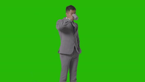 studio shot of businessman in suit holding and drinking cup of hot drink against green screen 2