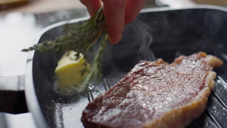 cooking steak with butter and rosemary in grill pan