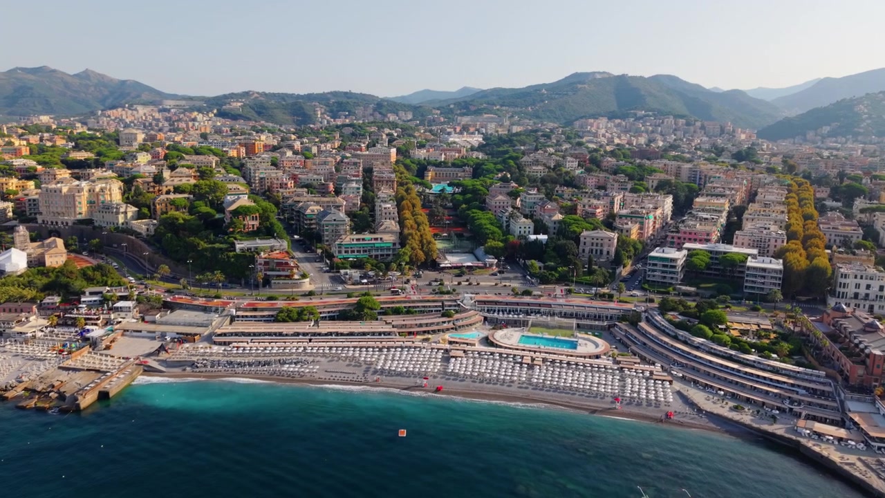 Vista aerea della costa di Genova con stabilimenti balneari, edifici cittadini e colline in estate