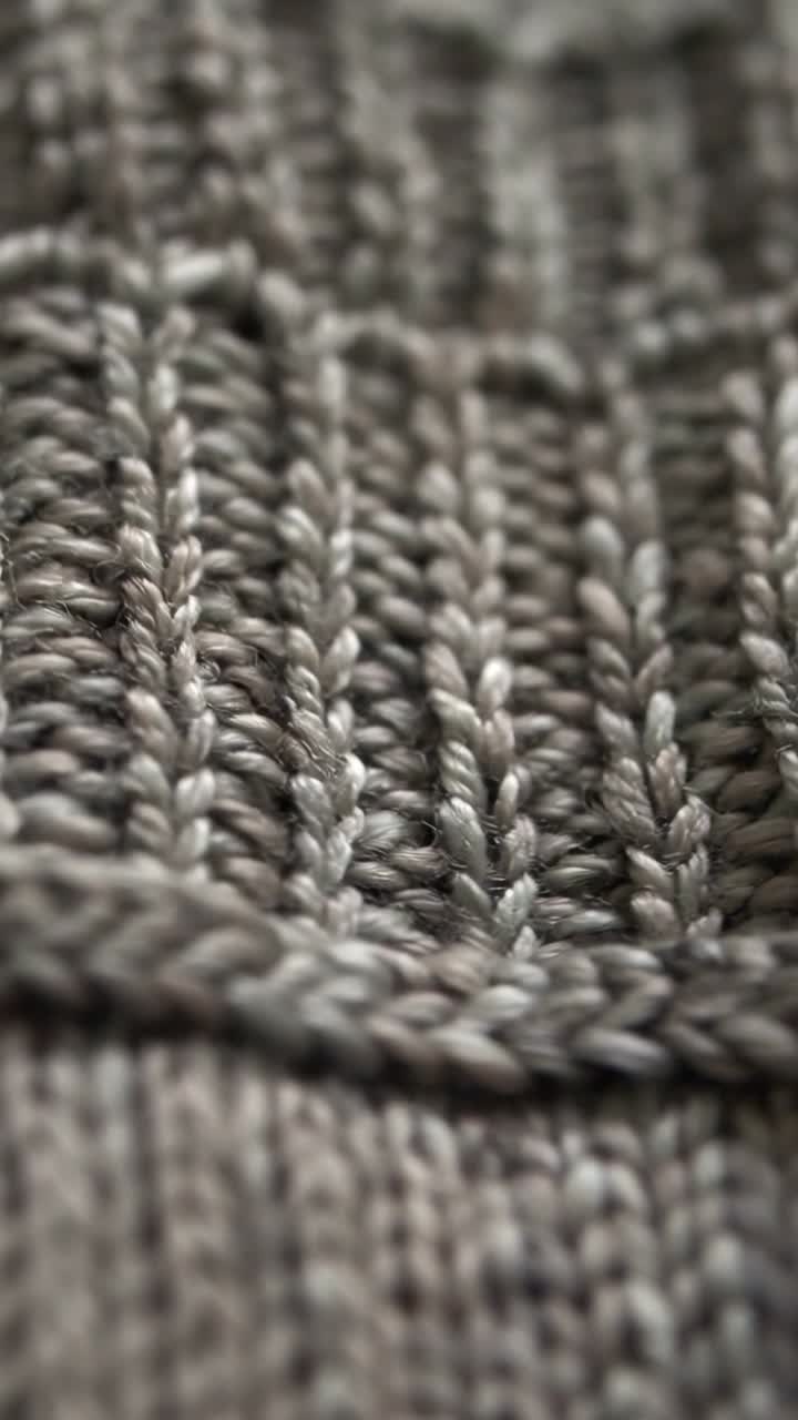 Vertical video: Starting camera panning across gray knit on table revealing rib and cable pattern