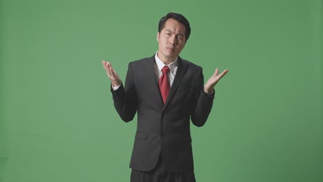 아시아 남성 사업가 혼란스러운 몸짓을 보여주고 녹색 화면 배경에 무엇을 말하는