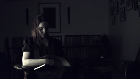 Mujer-Sentada-En-Una-Habitación-Oscura-Hojeando-Un-Libro-De-Fotografía-De-Mesa-De-Café