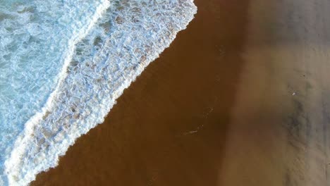 An-aerial-view-of-a-beach-with-cascading-waves-of-frothy-salt-water-tumbles-onto-the-sandy-beach