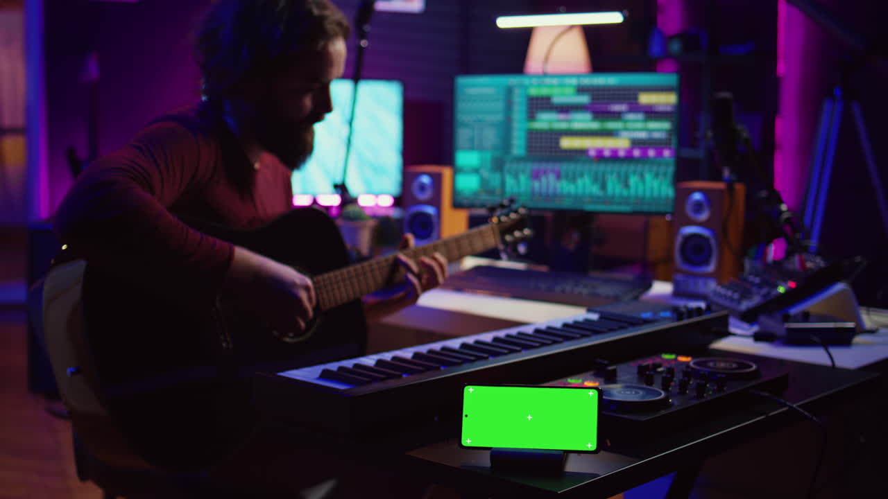 Songwriter playing acoustic guitar in home studio with greenscreen display