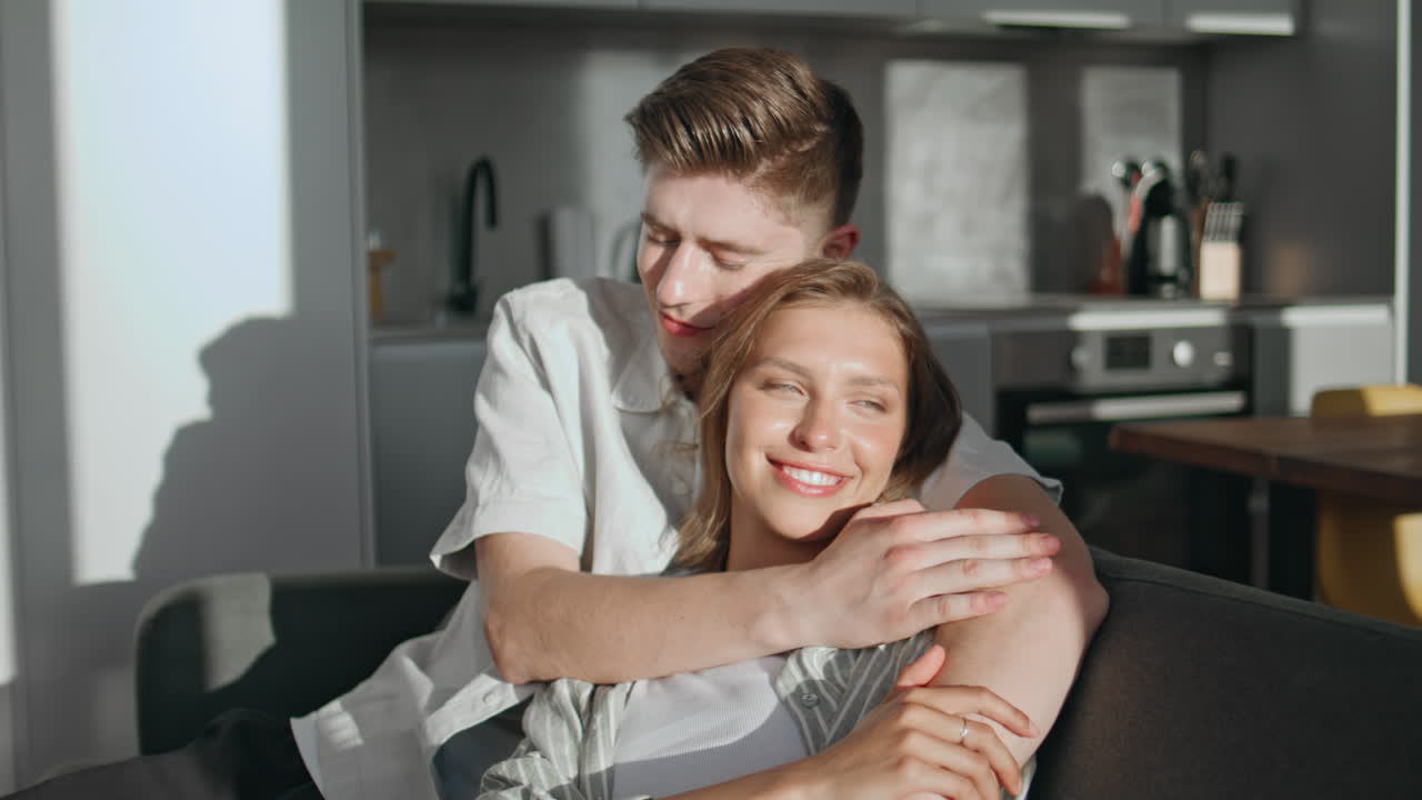 Happy sweethearts relax home in evening sunlight. Closeup loving man embracing