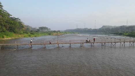 people crossing a bamboo bridge over a calm river