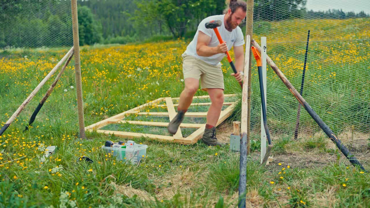 A Man Uses a Mallet to Drive a Wooden Fence Post Into the Ground - Medium Shot