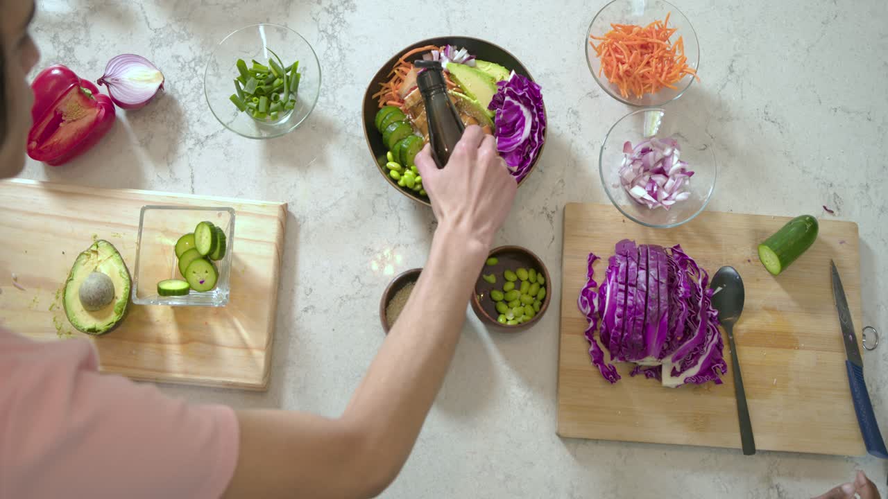 Casal diverso preparando salada na bancada, colocando abacate, espalhando sementes e regando com molho
