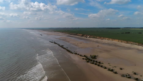 High-Establishing-Aerial-Drone-Shot-Over-Flat-Sandy-Beach-with-Rocks-and-Fields-behind-on-Sunny-Day-UK-East-Coast