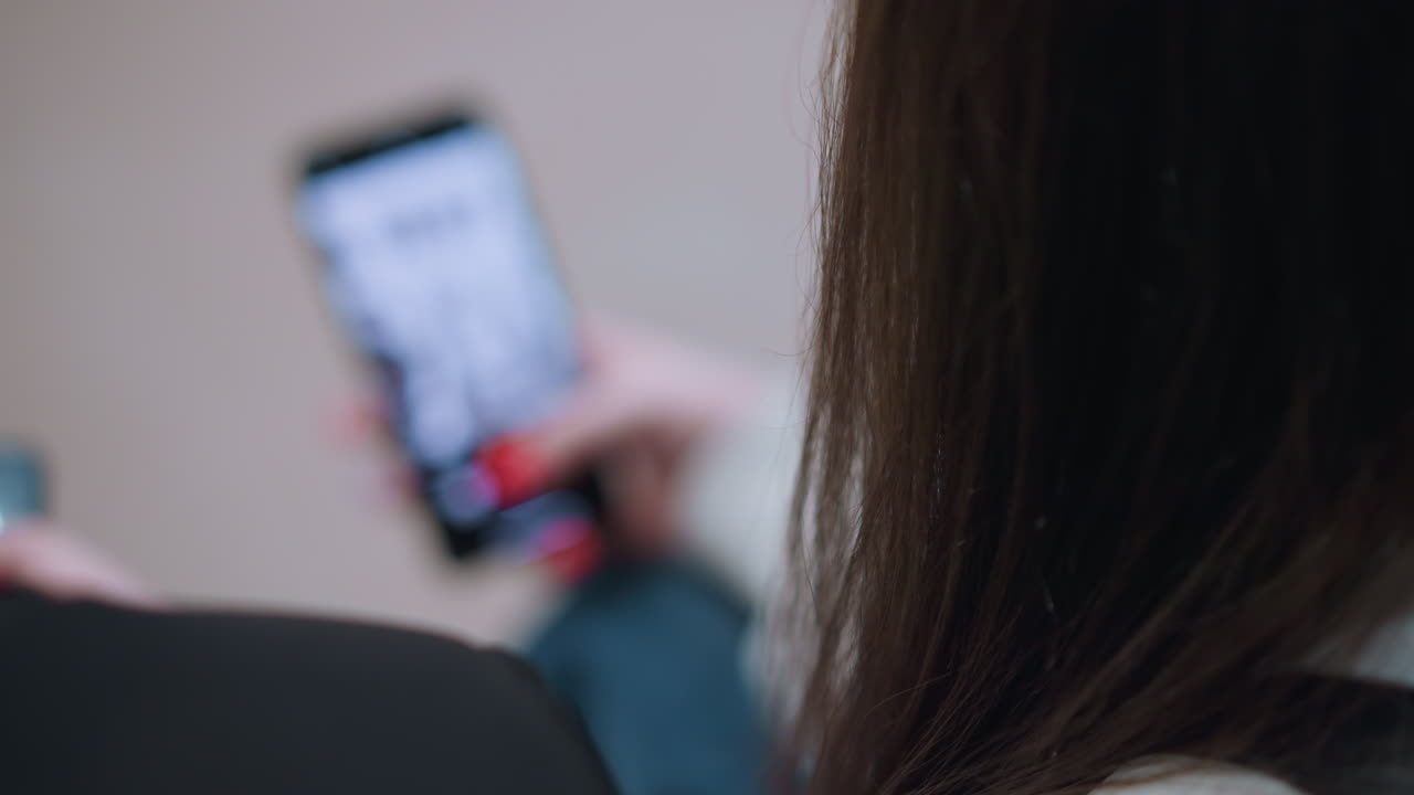 Close up rear view of person operating smartphone indoors, showing blurred perspective of hand holding mobile device with screen lit, representing modern digital lifestyle