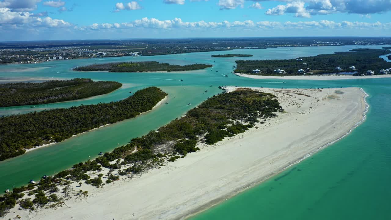 Grøn vegetation dækker kystøen flankeret af turkise vandveje og hvide sandstrande, med et udstrakt fastland i den fjerne baggrund under et blødt skydække