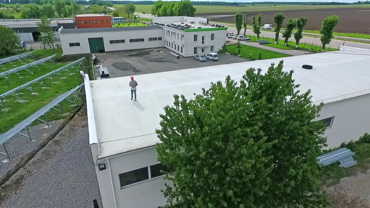 Worker in safety helmet on rooftop. Engineer standing on a flat roof of a big builduing in summer. Development of solar farm from roof. Aerial view.