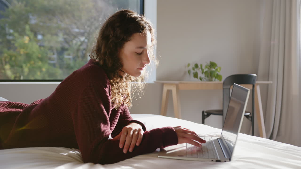 Lying on bed, woman using laptop and relaxing in cozy bedroom