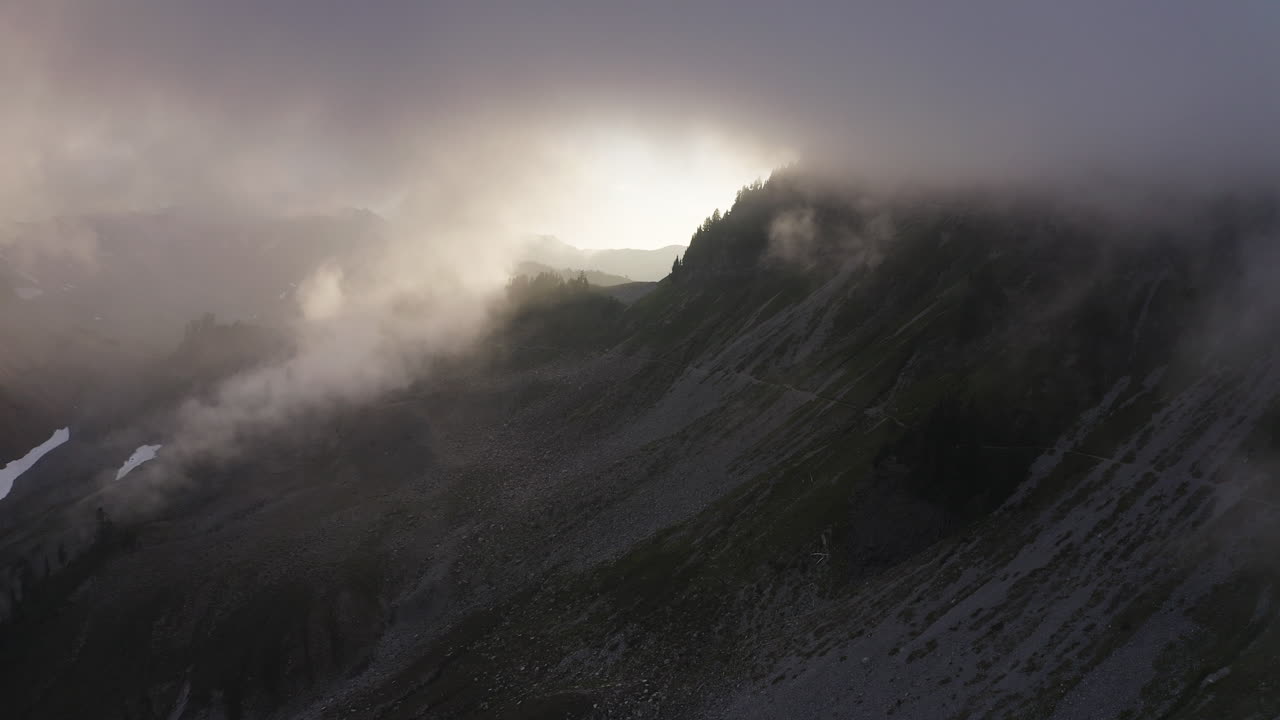 pendientes rocosas a la sombra de una espesa cubierta de nubes de niebla mientras la luz del atardecer aparece en el otro lado de la montaña