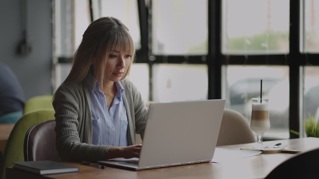 Young Asian attractive female office worker sitting at the laptop computer at the desk working and thinking. Mixed race woman working from home on laptop computer.