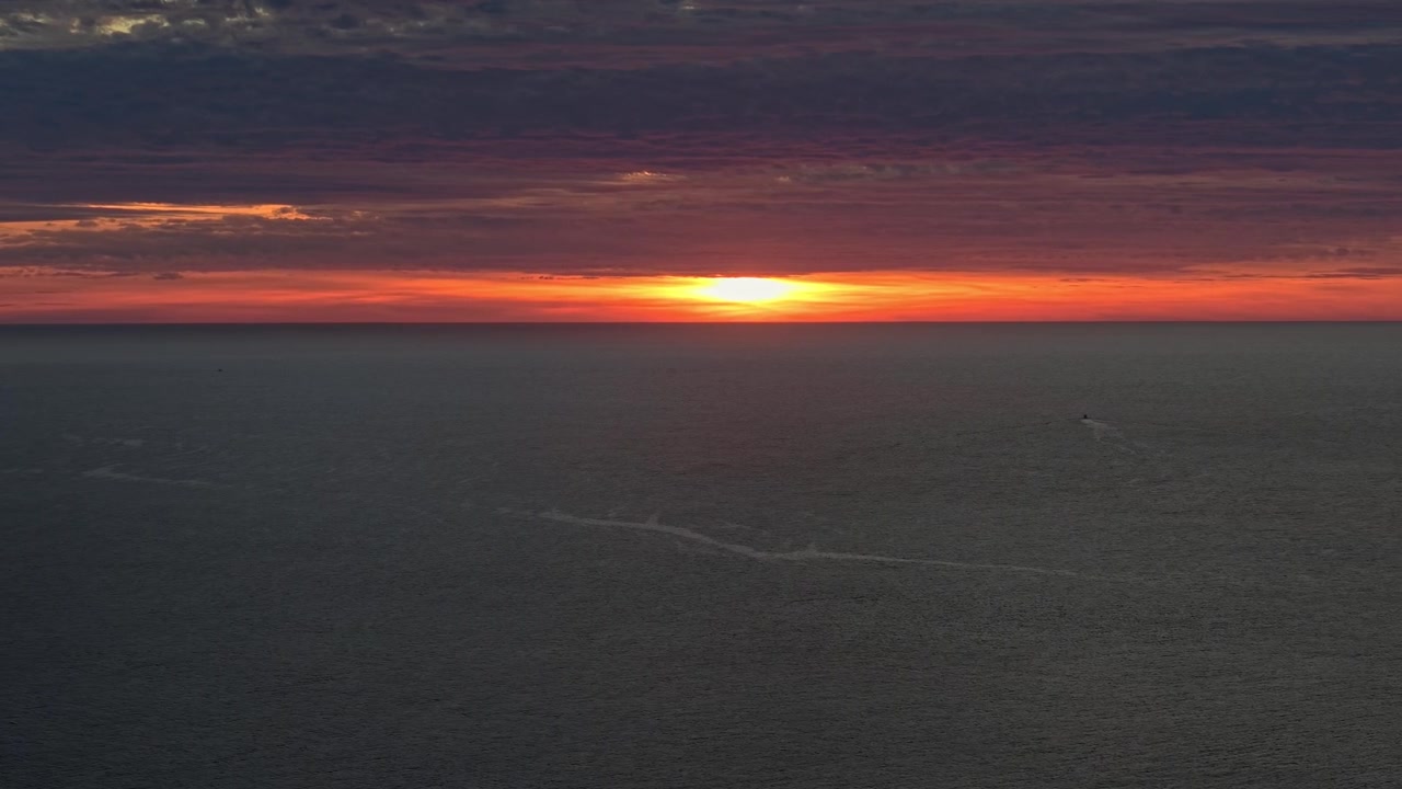 Une vue aérienne au téléobjectif d'un coucher de soleil solitaire projetant sa lueur sur l'horizon au-dessus de l'océan Pacifique.