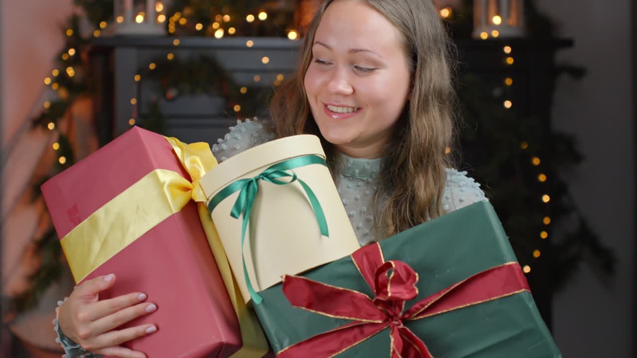 휴일의 마법이 포착되었습니다. 흥분된 여성은 파트너로부터 여러 가지 크리스마스 선물을 공개합니다.