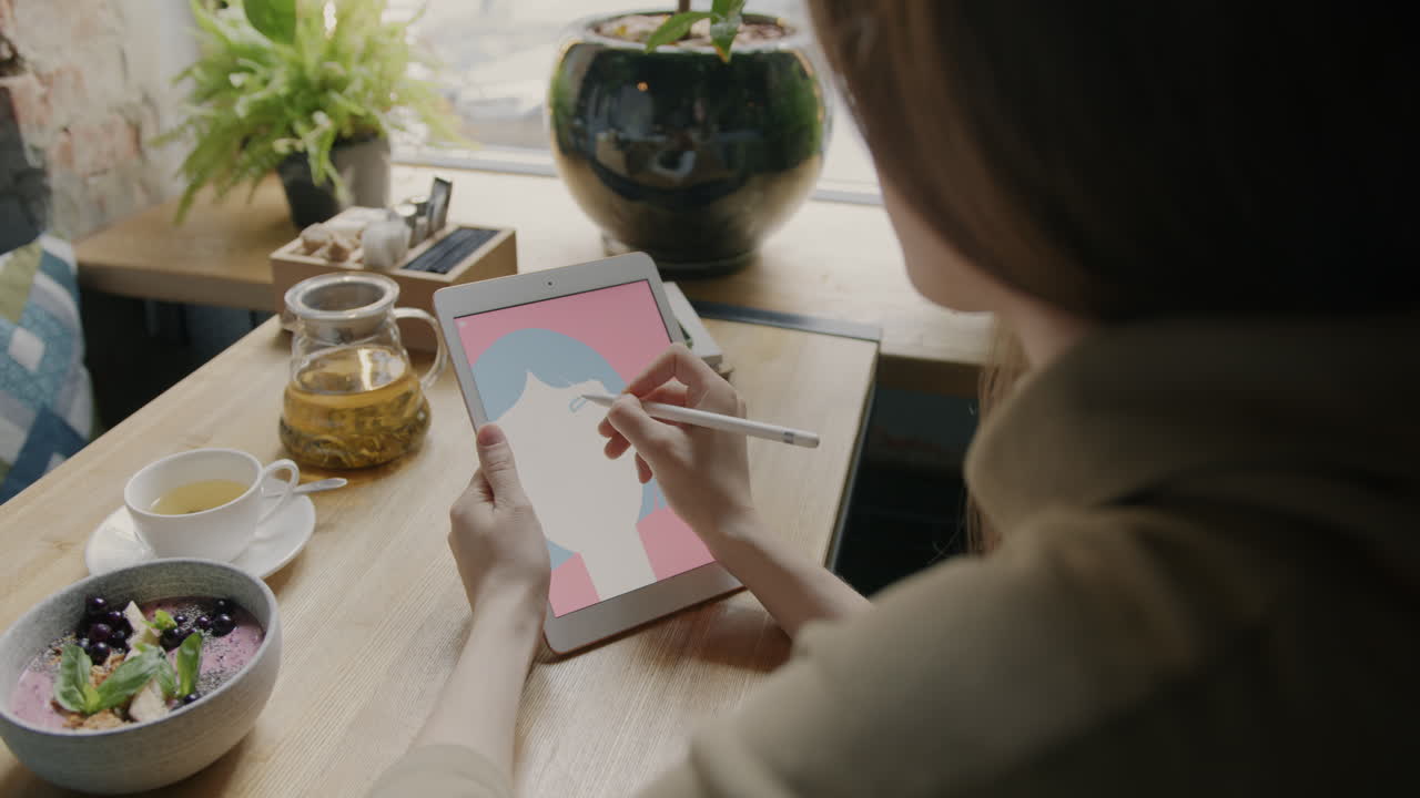 Woman Drawing a Portrait on a Tablet in a Cafe